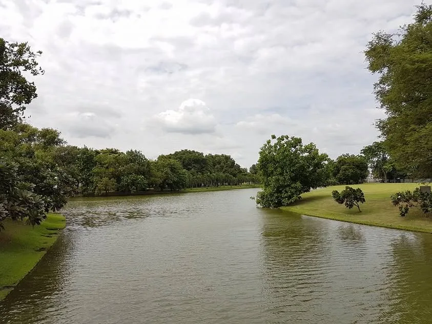 Still water reflects tall trees beside green lawns and dense garden planting.