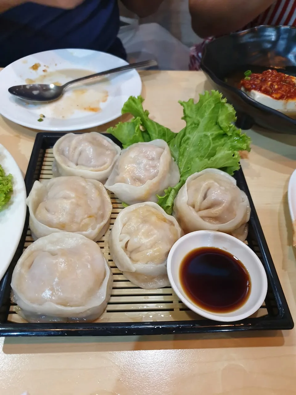 Round dumplings sit on a bamboo mat with lettuce and a bowl of dipping sauce.
